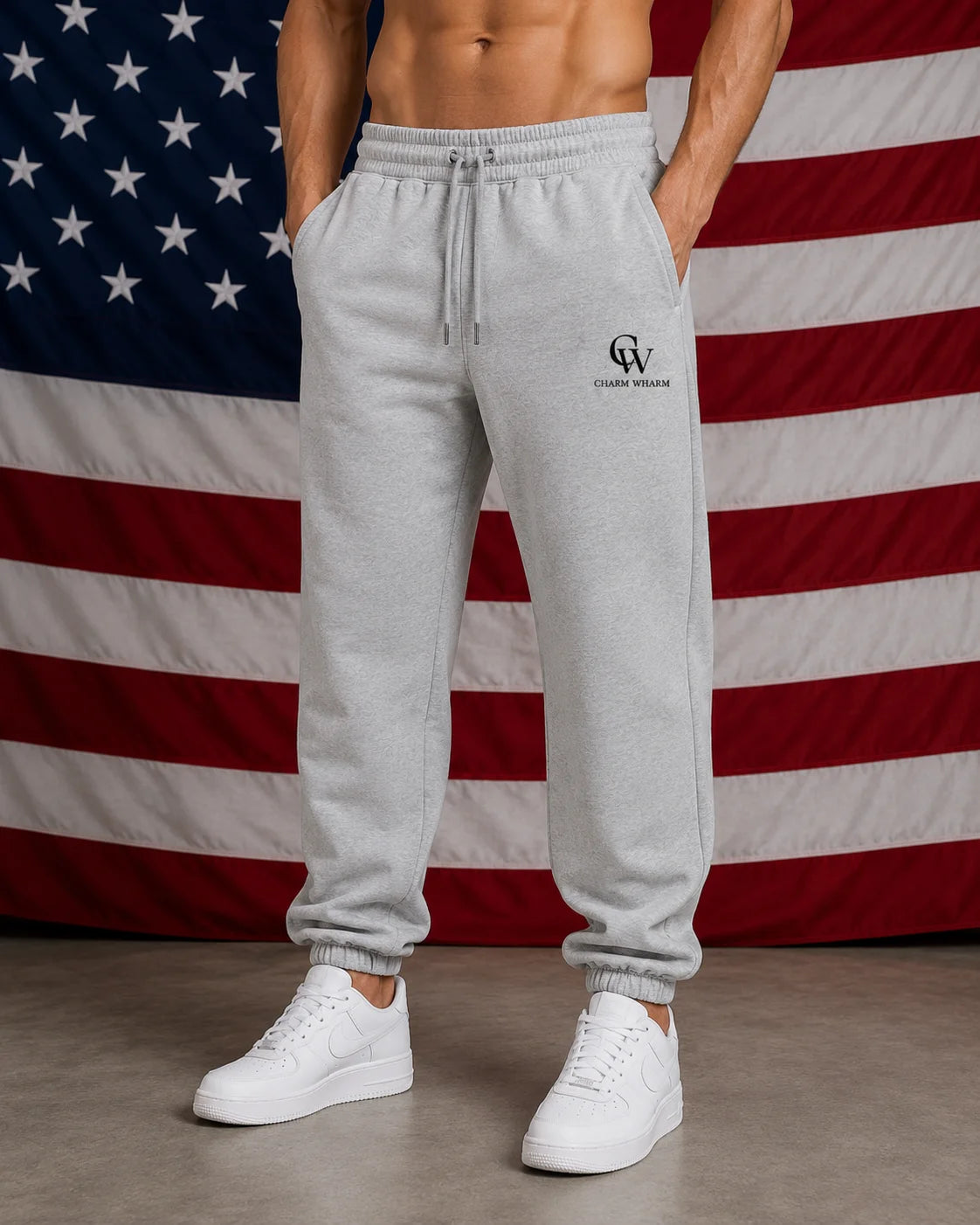 A man wearing light gray heather jogger sweatpants with a drawstring waist and elastic cuffs, standing in front of an American flag backdrop. The sweatpants have a small black 'CW' logo on the left thigh.