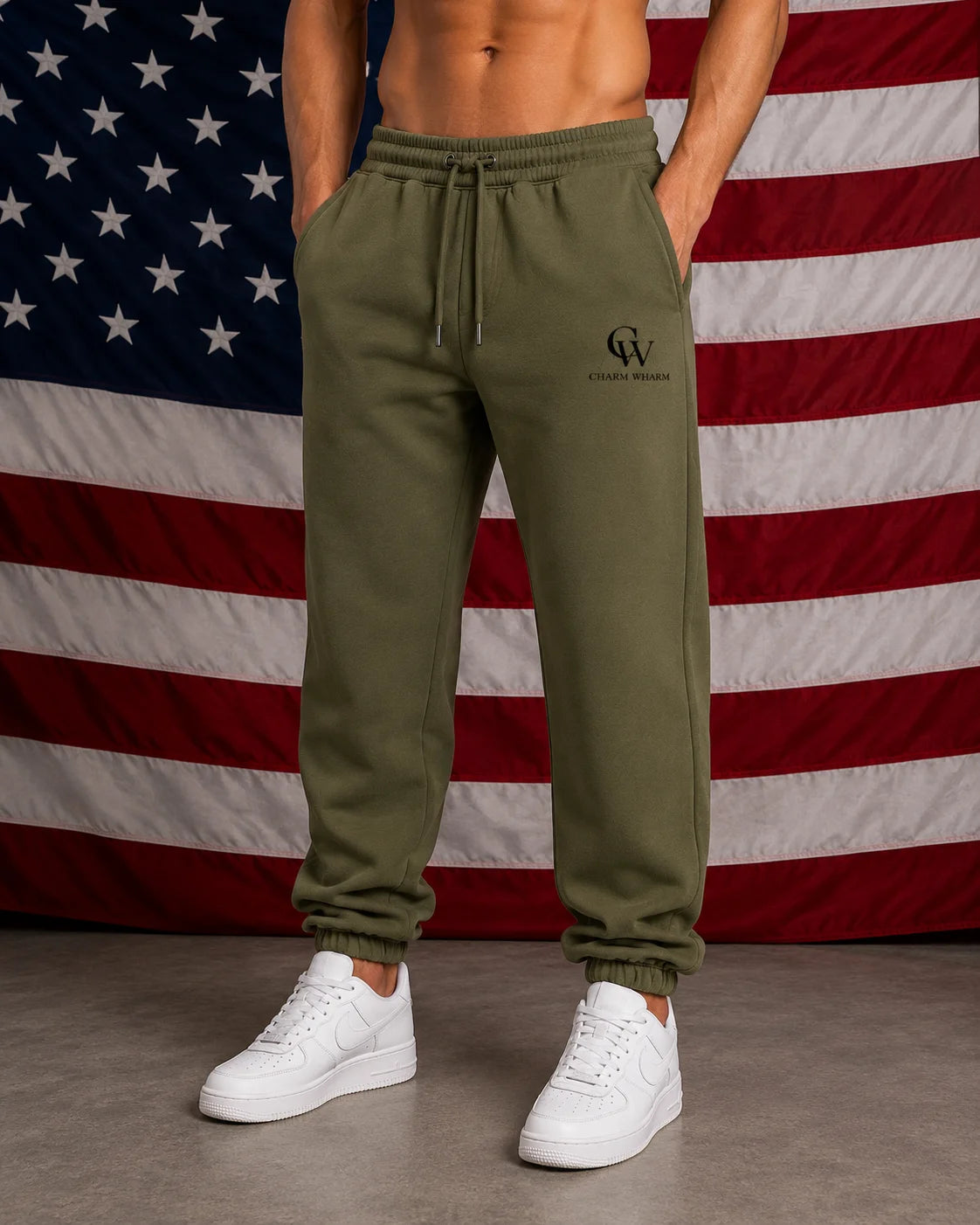 A man wearing olive green drawstring sweatpants with a black 'CW' logo on the left thigh, paired with white sneakers, standing in front of an American flag backdrop.