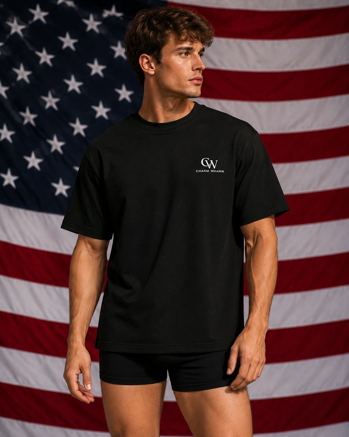 A man modeling a black short-sleeve crewneck t-shirt with a small white 'GW' logo on the left chest, paired with black shorts, set against a large American flag backdrop.
