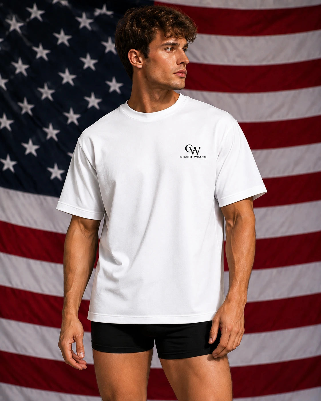 A man wearing a white crewneck t-shirt with a small black 'CW' logo and 'GREAT WALLS' text on the left chest, paired with black athletic shorts, standing in front of a large American flag backdrop.